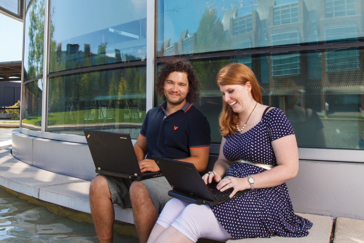 There are two people using their laptops on a sunny day and while cooling off their feet in reflection pool.