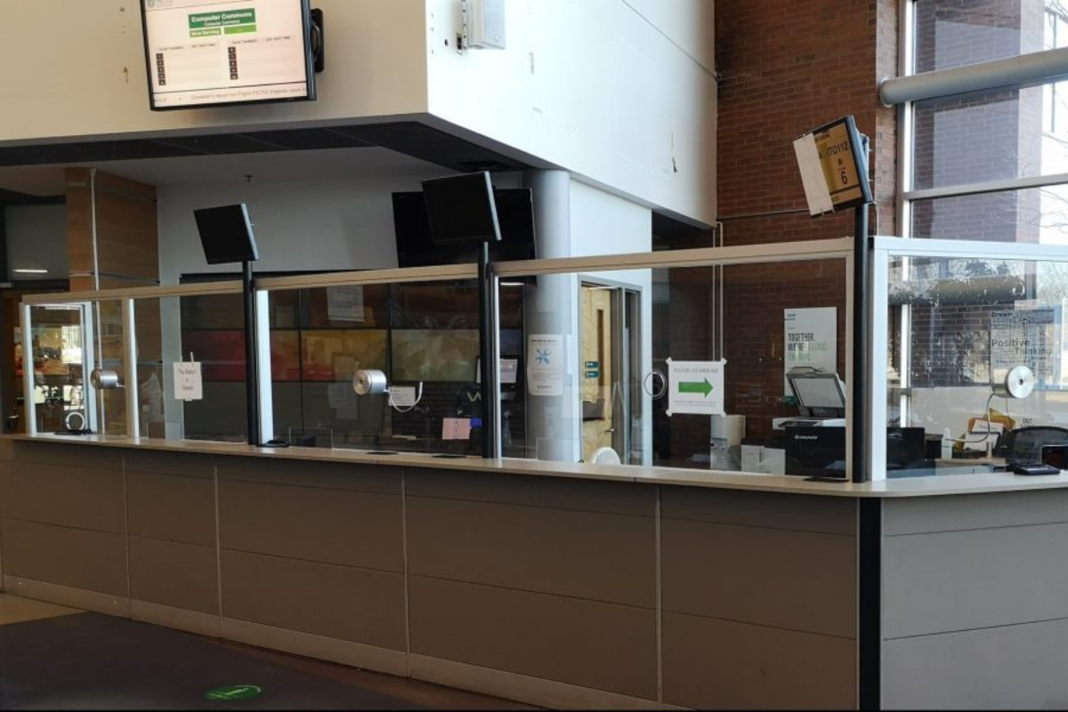 A service counter that stretches across the frame and is enclosed by a glass partition, which separates the customer-facing area from the staff workstations. 