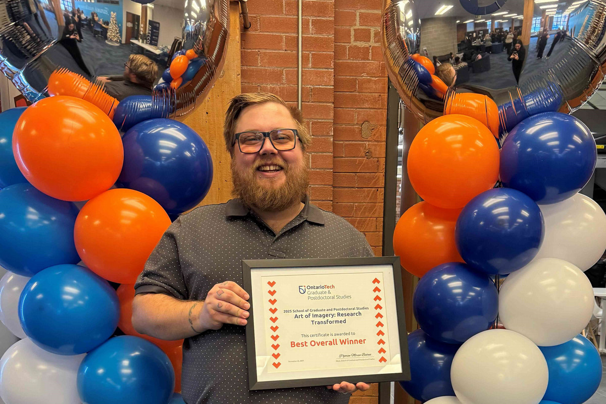 young graduate student holding best overall certification with Ontario tech coloured balloons