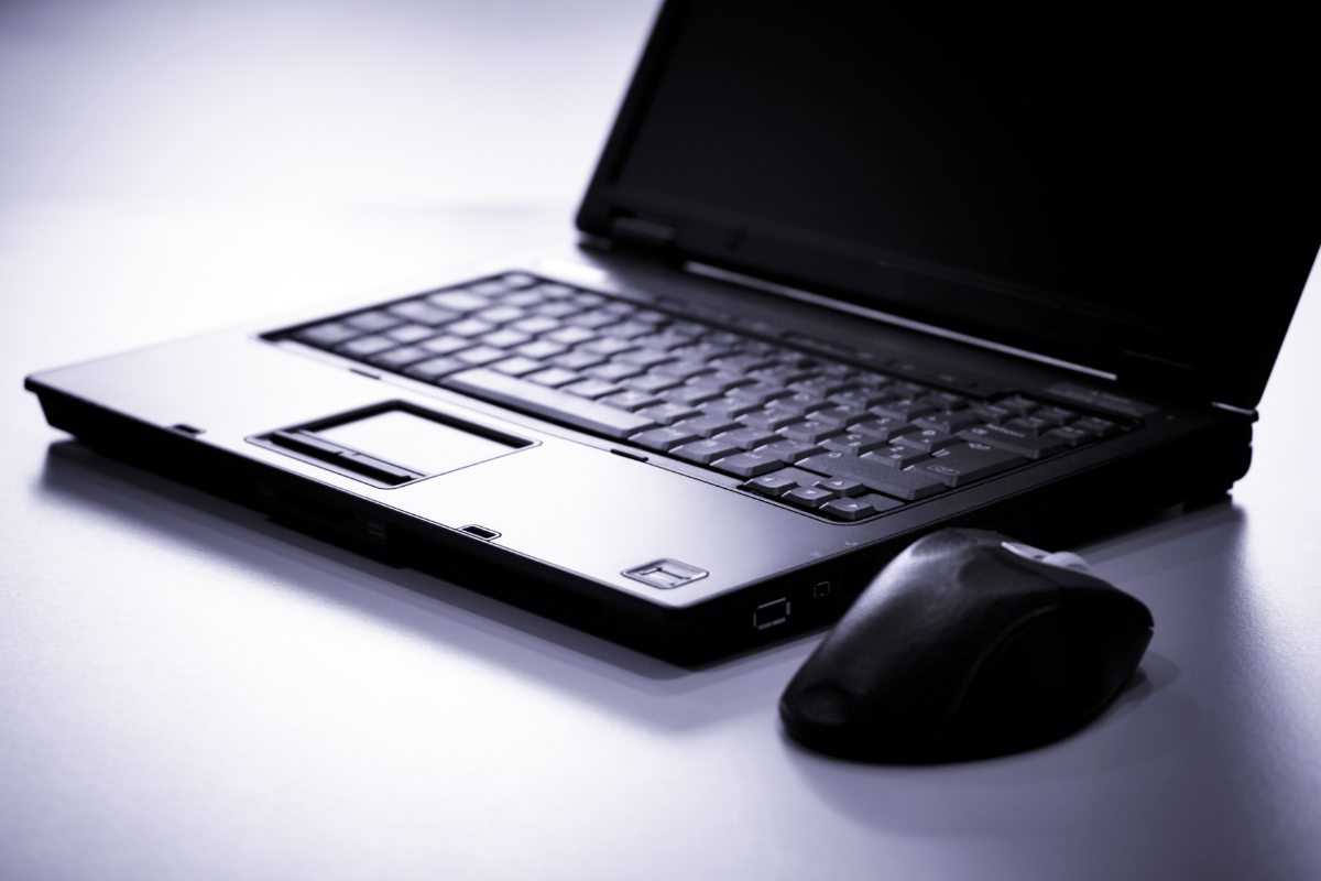Black laptop sitting open on a table, with a mouse sitting next to it.