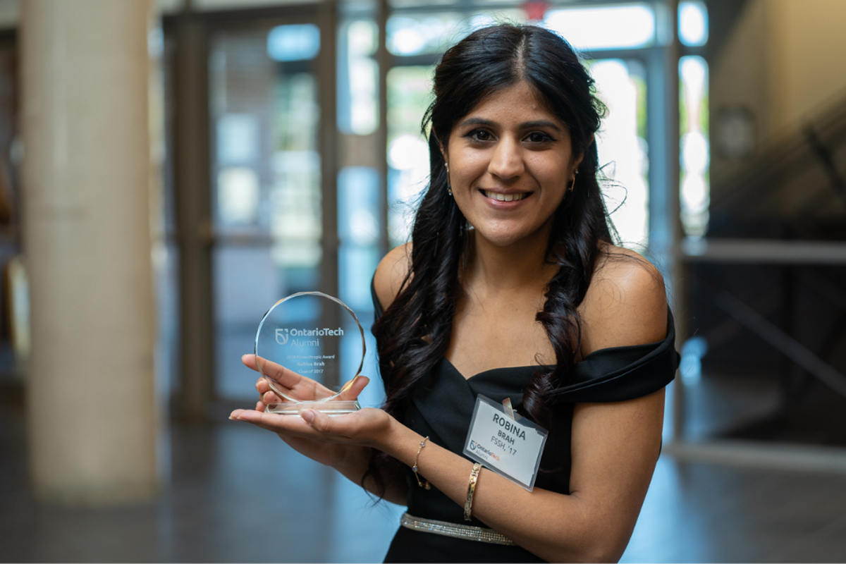 Woman holding a glass circular award that says Ontario Tech Alumni