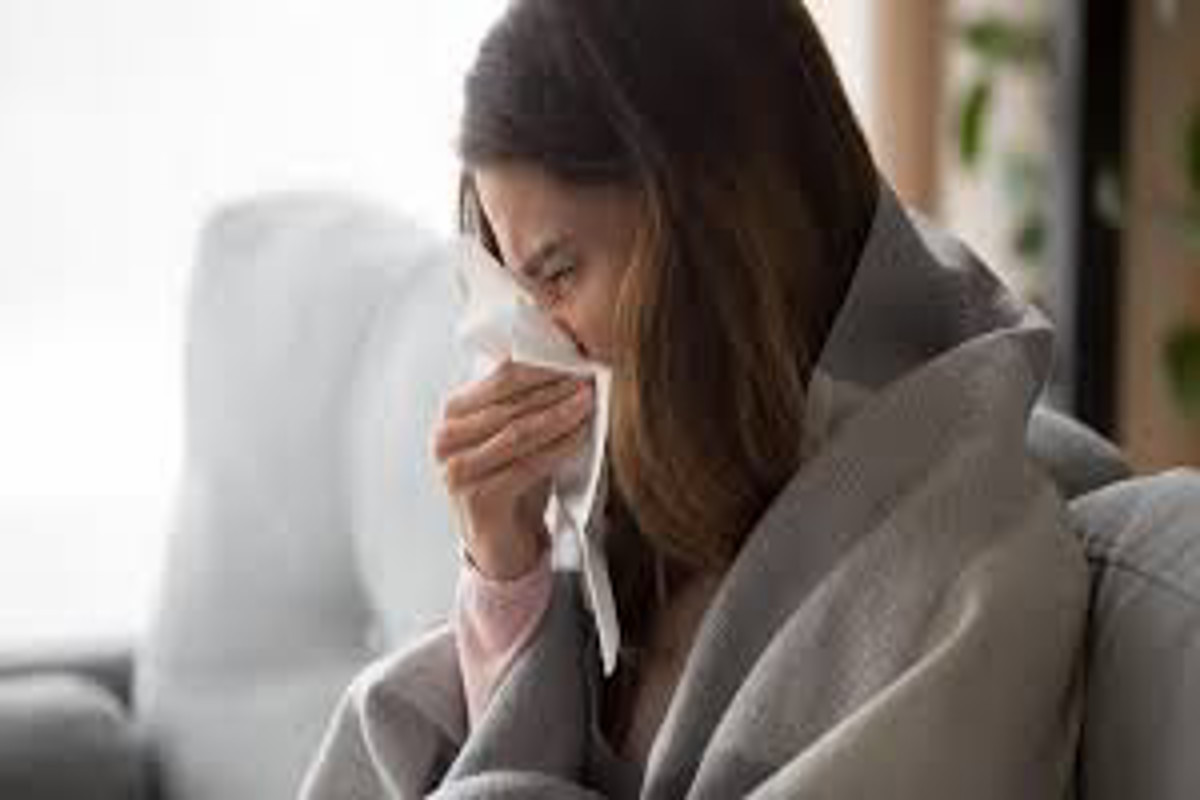 Woman covered in a blanket blowing her nose.